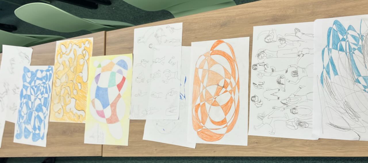 many pieces of paper lined up on a table. Each piece has a drawing, which is alaternating regions of white and color.
