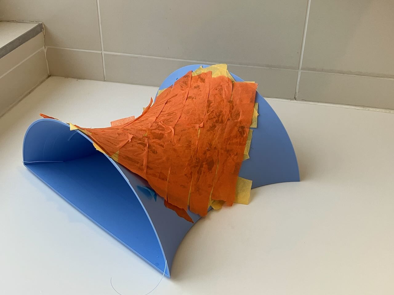 A saddle-shaped 3D printed mold, with orange and yellow tissue paper layered on top 