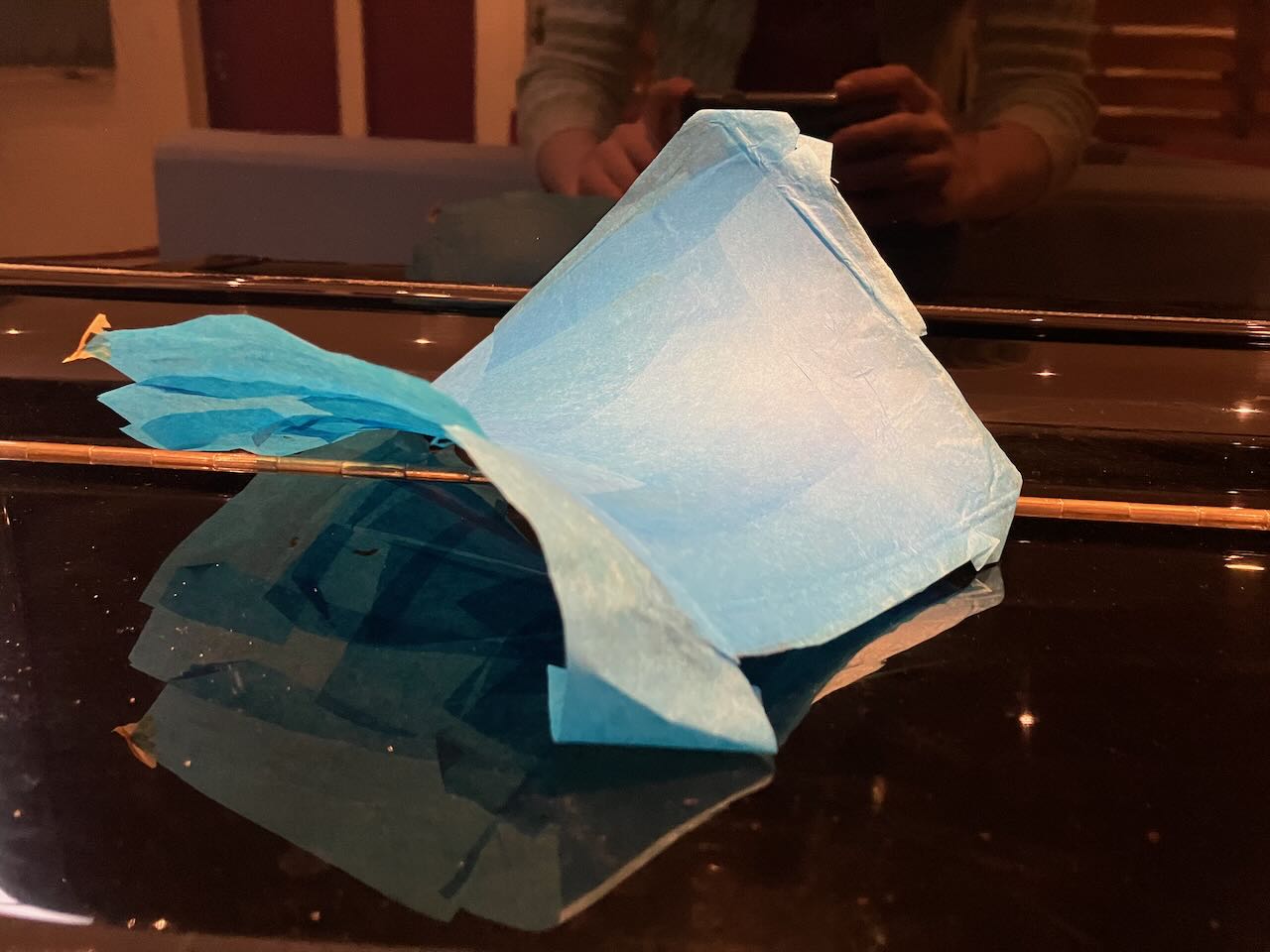 A blue sheet of paper conforming to a saddle shape, laying on a glossy black surface 